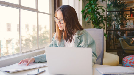 Young Businesswoman Wearing Glasses At Desk Working On Laptop In Modern Office