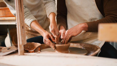 Close Up Of Female Teacher Helping Man Sitting At Wheel In Pottery Classの写真素材