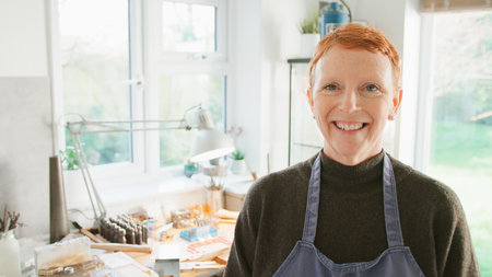 Portrait Of Smiling Female Jeweller At Bench Working In Studioの写真素材