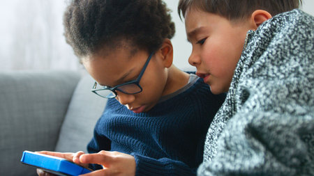 Two Boys Gaming Together On Hand Held Device At Home