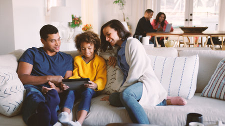 Multi Generation Family At Home With Parents And Daughter Using Digital Tablet In Foregroundの写真素材