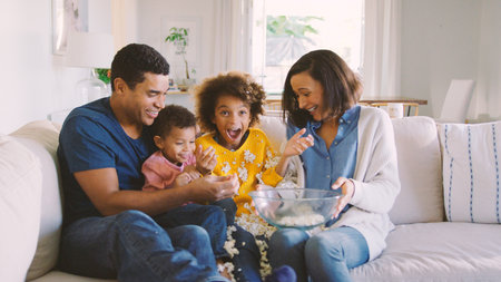 Family At Home Sitting On Sofa Watching TV And Spilling Popcorn Togetherの写真素材