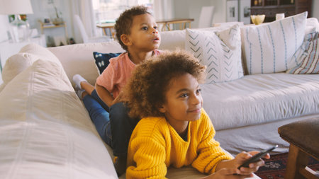 Brother And Sister Lying On Sofa At Home Watching TV Togetherの写真素材