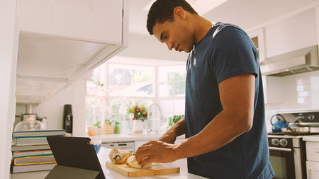 Man In Kitchen Preparing Meal Following Online Recipe On Digital Tabletの写真素材