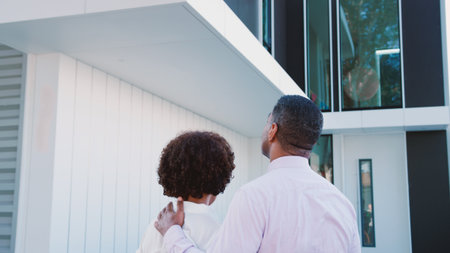 Rear View Of Mature Couple Standing And Looking Up At Houseの写真素材