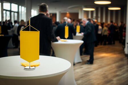 People in conference hall at background, table on the first plan with yellow flag