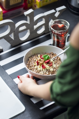 Breakfast with chocolate oatmeal prepared by a woman, puffed rice, cereals, dried strawberries in white bowl and green teaの写真素材