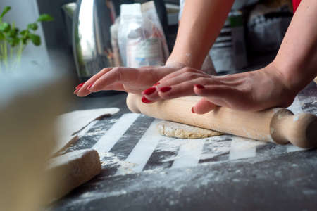 Woman rolling dough for pasta at the wooden table, she have nice red nails.の写真素材