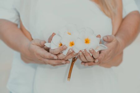 Engagement at the beach of tropical island. Hands of couple with golden ring on the finger and flowersの写真素材
