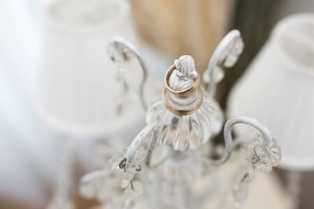 Golden wedding rings placed on a white candlestick illuminated by morning lightの写真素材