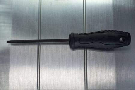 Professional reinforced black matt screw driver placed on a polished aluminum surface. View from the top.の写真素材
