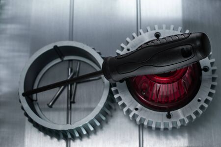 Professional reinforced black matt screw driver placed on a gearwheel. View from the top.