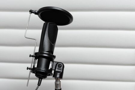 Condenser microphone placed on a tripod with white acoustic panels in the background in a music studio, ready for recording.の写真素材