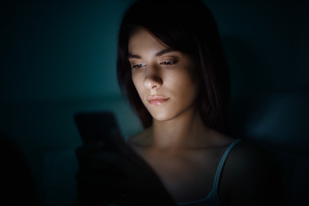 Woman with smartphone in the night on bedの写真素材