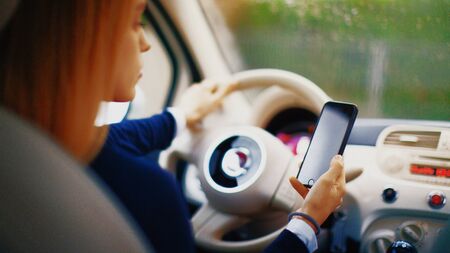 Young blonde woman in her new car smiling. Use the smartphone in the car