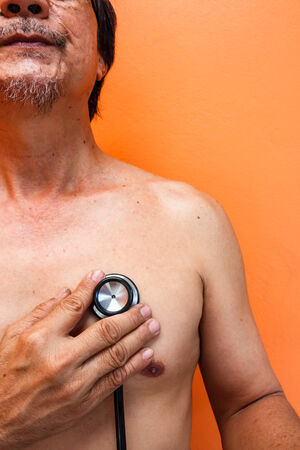 old aged asian man was diagnosed by doctor on orange backgroundの写真素材