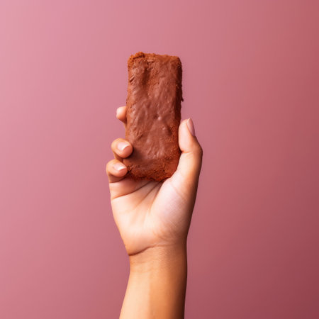 the chocolate bar in this photo is held tightly by a hand against a vibrant pink background. the exciting texture of the chocolate is highlighted by the soft-edged style of the image. the meatpunk and raw feel of the photo adds a powerful element to the overall aesthetic. the cheese-like texture of the chocolate bar is emphasized, making it look even more delicious. this photoの素材