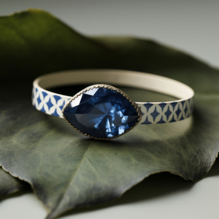an elegant blue bangle with a blue stone, captured in a tabletop photography style. the detailed foliage surrounding the bangle adds a touch of nature. the dark navy and light beige colors create a striking contrast. inspired by the northwest school, this piece showcases radiant colors and an asymmetrical design, with a singular focus on the beautiful blue stone. ai generatedの素材