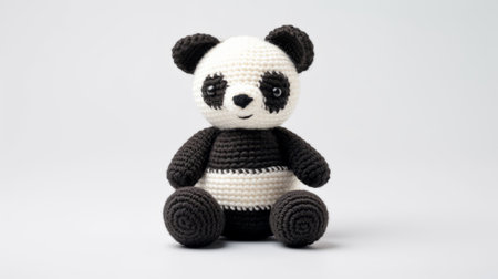 a small panda bear crocheted in black and white, showcasing harmonious coloration and toy-like proportions. this adorable creation combines traditional techniques with a modern twist, featuring a monochromatic color scheme of dark brown and light black. the bold color blocks stand out against the white background, making this crocheted panda a charming and eye-catching piece. ai generatedの素材