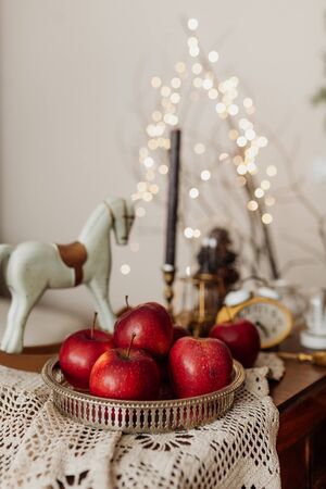 Christmas decorations. Red apples, wooden horse, candles, clock and lights on wooden table. Living room interior and holiday home decor conceptの写真素材