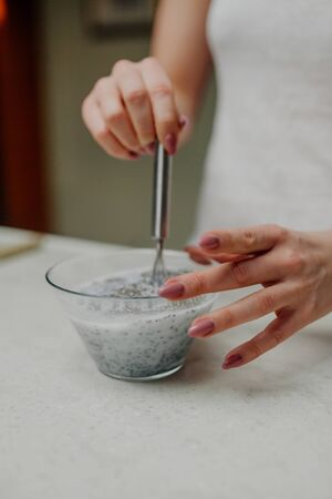 Close Up Woman Hands Mixing of Chia Pudding in Glass Bowl in Kitchenの写真素材