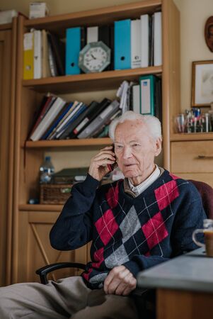 Elderly man talking on phone sitting at homeの写真素材