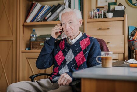 Elderly man talking on phone sitting at homeの写真素材