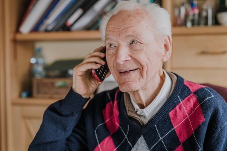 Elderly man talking on phone sitting at homeの写真素材