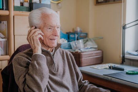 Elderly man talking on phone sitting at homeの写真素材