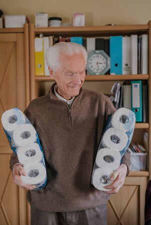 Old man holding two packs of toilet paperの写真素材