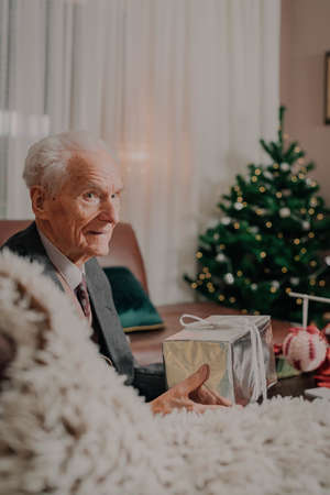 Senior Man Holding Christmas Gift in Hands on Christmasの写真素材