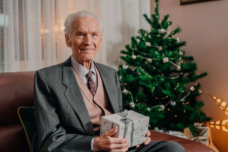 Senior Man Holding Christmas Gift in Hands on Christmasの写真素材