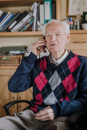 Elderly man talking on phone sitting at homeの写真素材