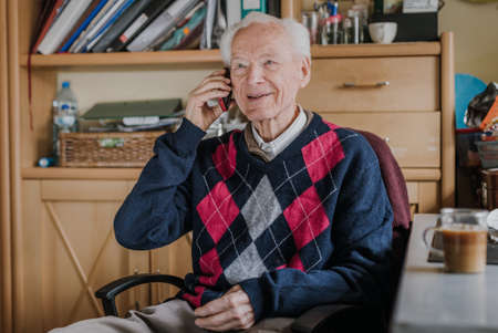 Elderly man talking on phone sitting at homeの写真素材