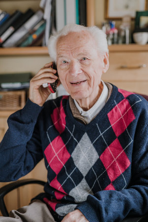 Elderly man talking on phone sitting at homeの写真素材