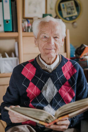 Old man looking at old albums with family photosの写真素材
