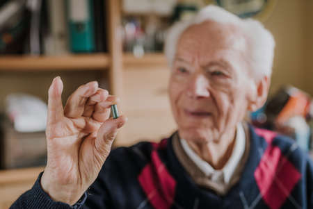 Old man holding one green tablet in hand closeup