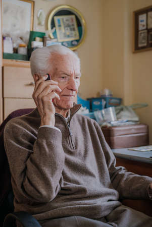Elderly man talking on phone sitting at homeの写真素材