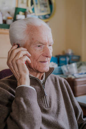 Elderly man talking on phone sitting at homeの写真素材