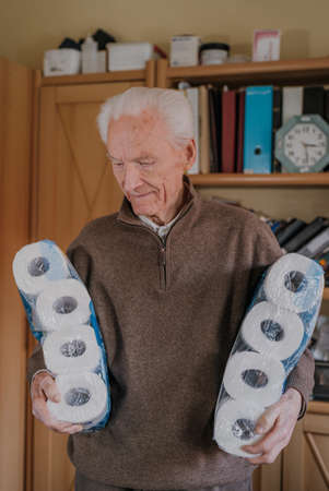 Old man holding two packs of toilet paperの写真素材