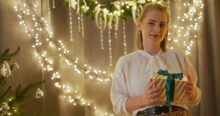 Happy Woman Opening a Present Against the Background of Shining Christmas Lightsの写真素材
