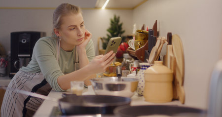 Woman Works in the Kitchen and Browses the Internet on Her Smartphoneの写真素材
