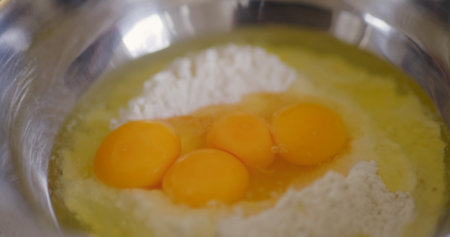 Raw eggs cracked into flour in bowlの写真素材