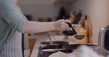 Woman Scooping Pancake Batter with Ladle in Kitchen While Cookingの写真素材