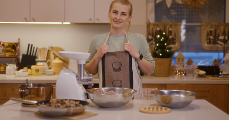 Woman smiles in kitchen background while working preparing holiday dishesの写真素材