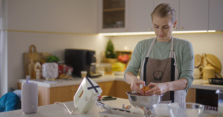 Woman cracks raw egg into bowl of flour and prepares dough for bakingの写真素材