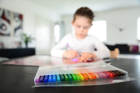 Creative kid sitting at the living room table drawing with her colorful markersの写真素材