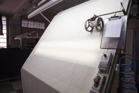 white fabric sliding over a quality controll lamp. with a counting machine measuring the length of a textile piece /roll. production of fine woolen fabrics for suits - in a factory in Sabadell, Spainのeditorial素材
