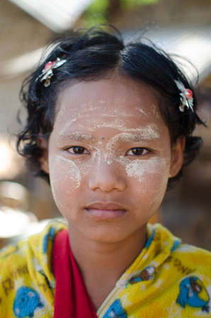 A girl wears traditional Thanaka on her face at her family's small snack shop on in Bagan, Mtanmar Burma. The traditional Thanaka paste is believed to cool the skin, tightens the pores and controls oiliness.のeditorial素材