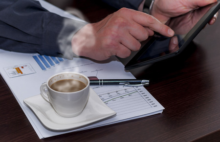 Man works in bussiness office with computer or laptop or notebook and papper graf and he drinks coffeeの写真素材